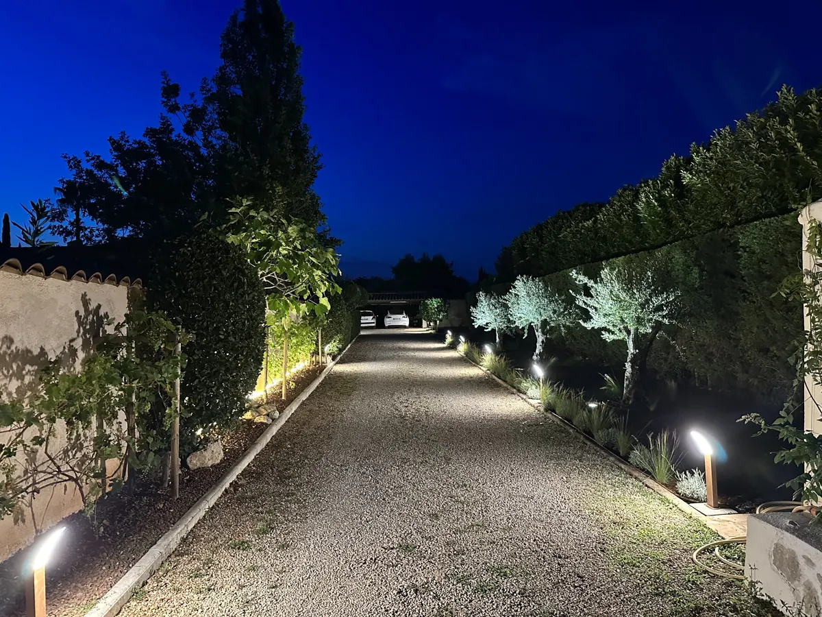 Allée de villa éclairée par des bornes, haies et arbres en lumière